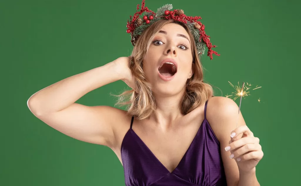 magic woman in front of green wall holding a sparkler. Mouth open 