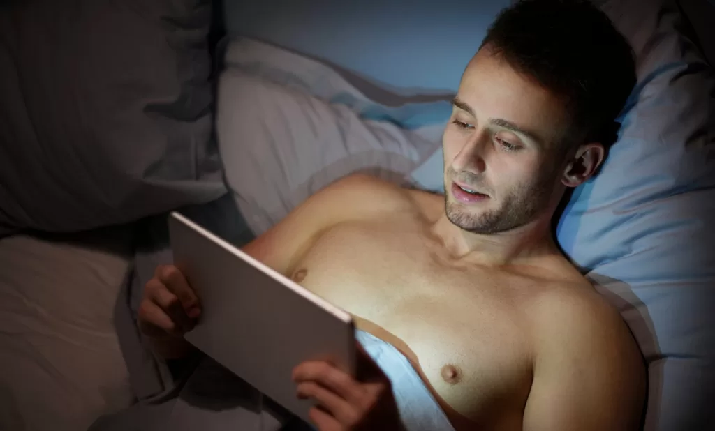 man in bed with tablet comparing Erome vs Clip4Sale